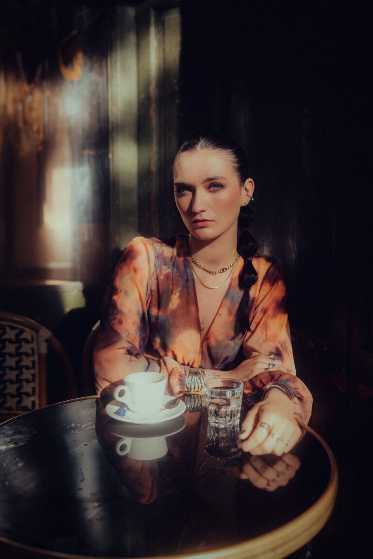 Maquillage regard intense et naturel pour femme brune aux yeux bleus qui boit un café en terrasse