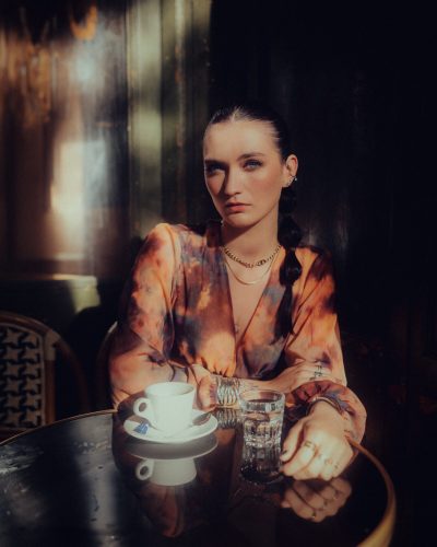 Maquillage regard intense et naturel pour femme brune aux yeux bleus qui boit un café en terrasse